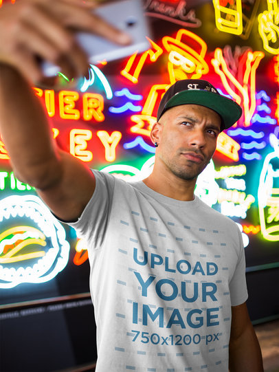 T-Shirt Mockup of a Black Man Taking a Selfie Against Neon Signs